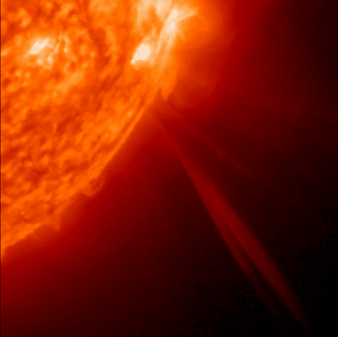 A bright orange-red bottom right corner of the sun, with a long whisp of red soaring out into space